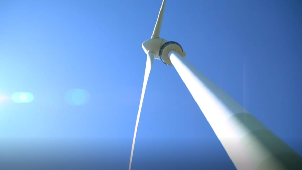Ausschnitt aus dem Video mit einem Windrad von unten und gegen die Sonne aufgenommen.