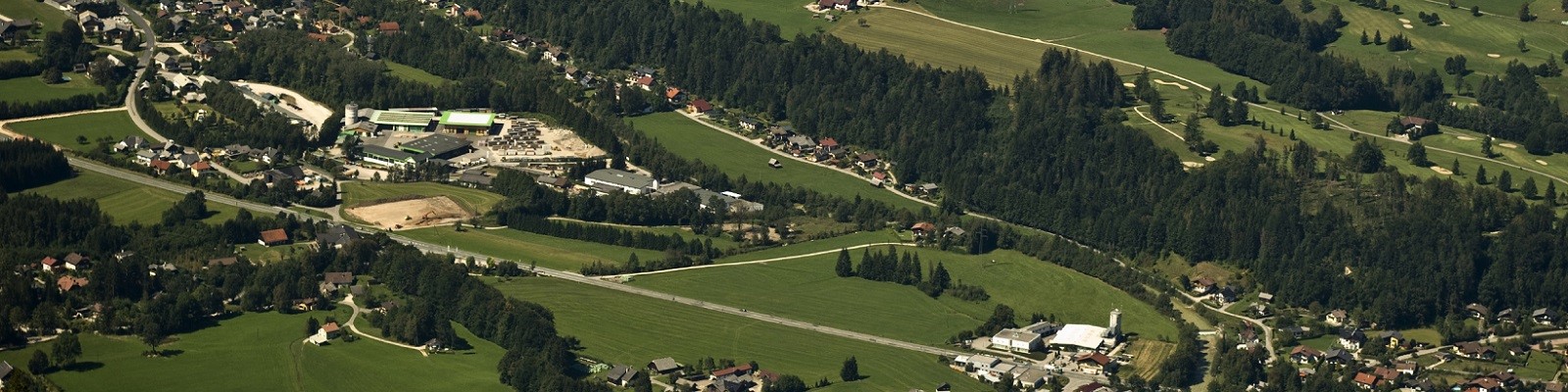 Das Luftbild zeigt das Umland einer österreichischen Kleinstadt mit Gewerbegebiet, Wohn- und Grünflächen und Wald.