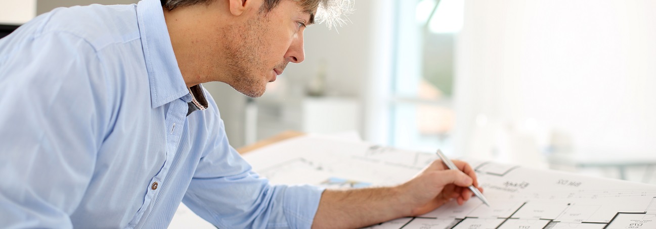 Männlicher Architekt zeichnet mit der Hand auf einem Grundrissplan, ein Symbol für förderfähige Bauprojekte. 