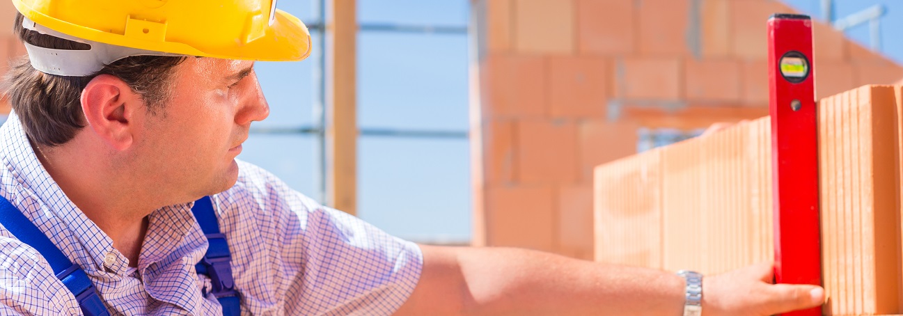 Foto eines Bauarbeiters der eine Wasserwaage an einer Mauer anlegt