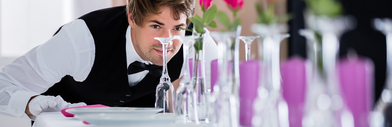 Foto eines Kellners beim Ausrichten von Gläsern einer gedeckten Tafel